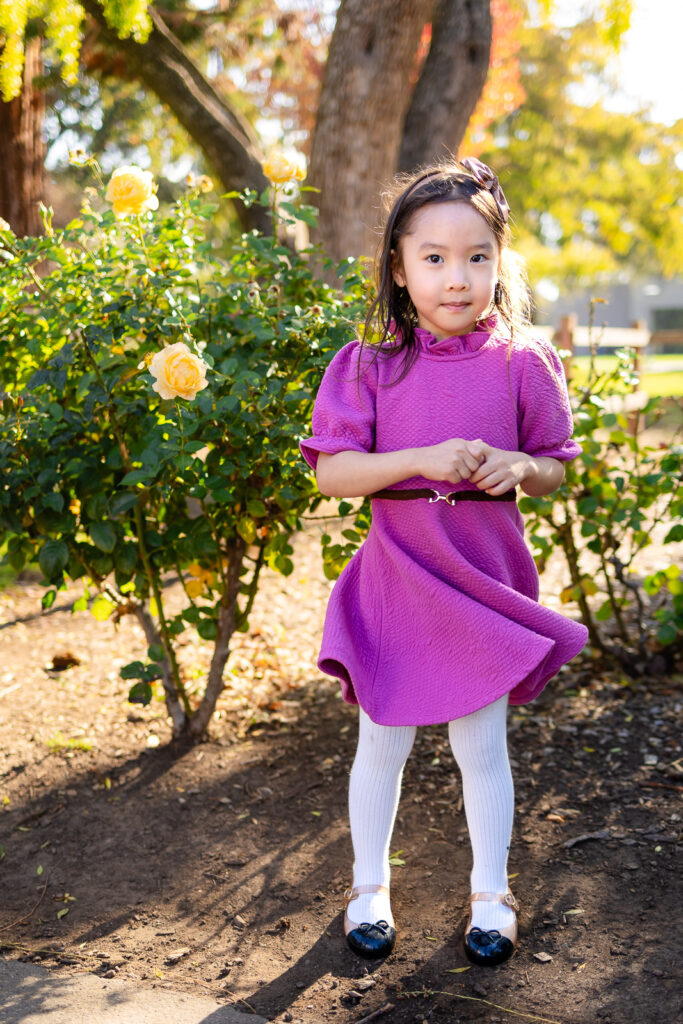 Young girl standing by yellow rose bushes in a park for guidance for a relaxed family photoshoot
