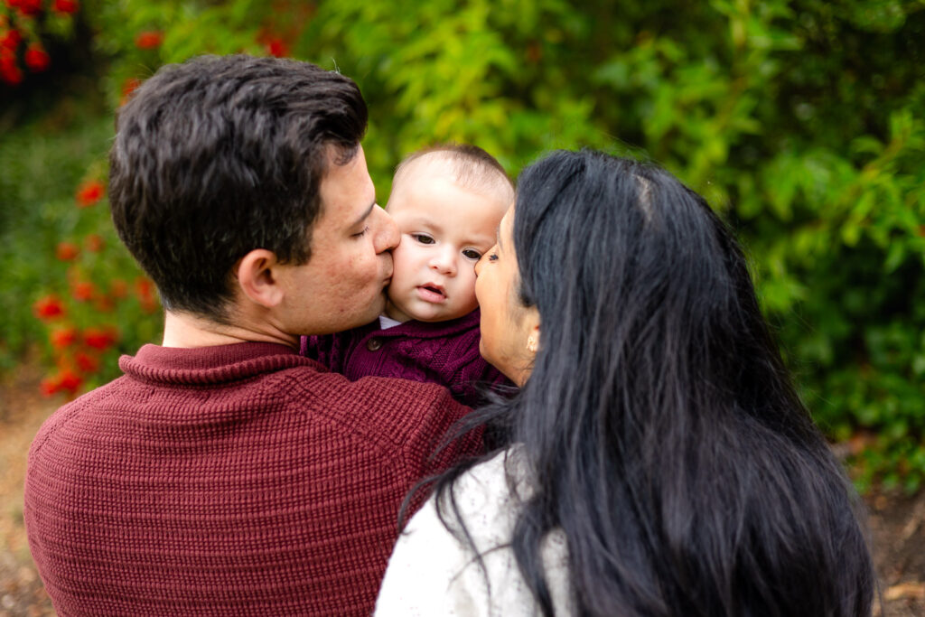 Parents kissing their baby’s cheeks during a playful moment at Millbrae Meadows Park