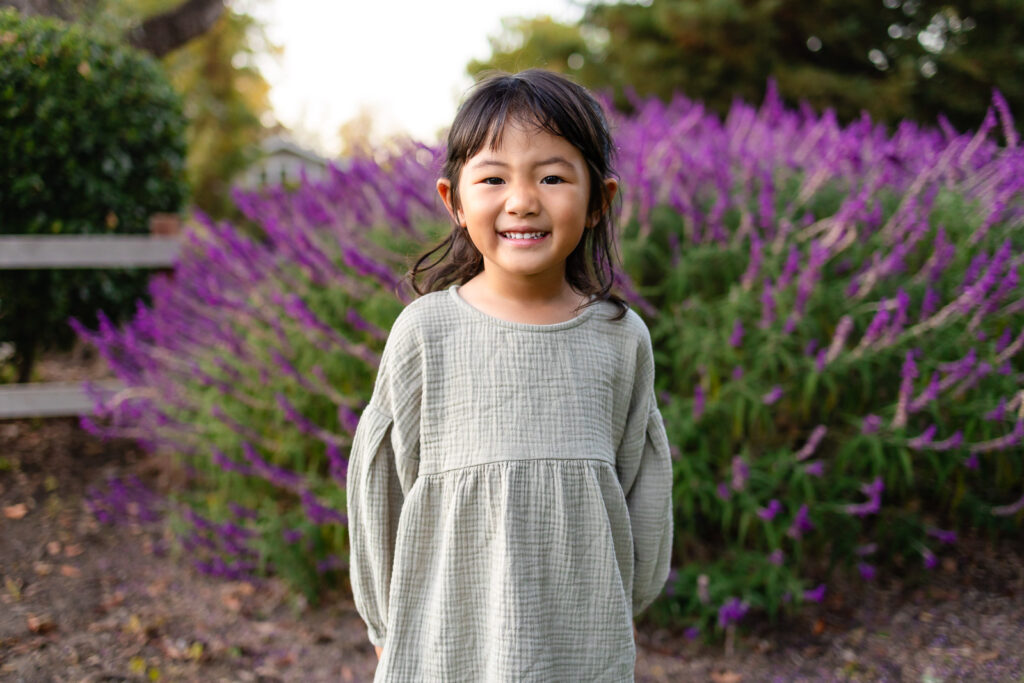 Child smiling with purple blooms behind her in a Bay Area park