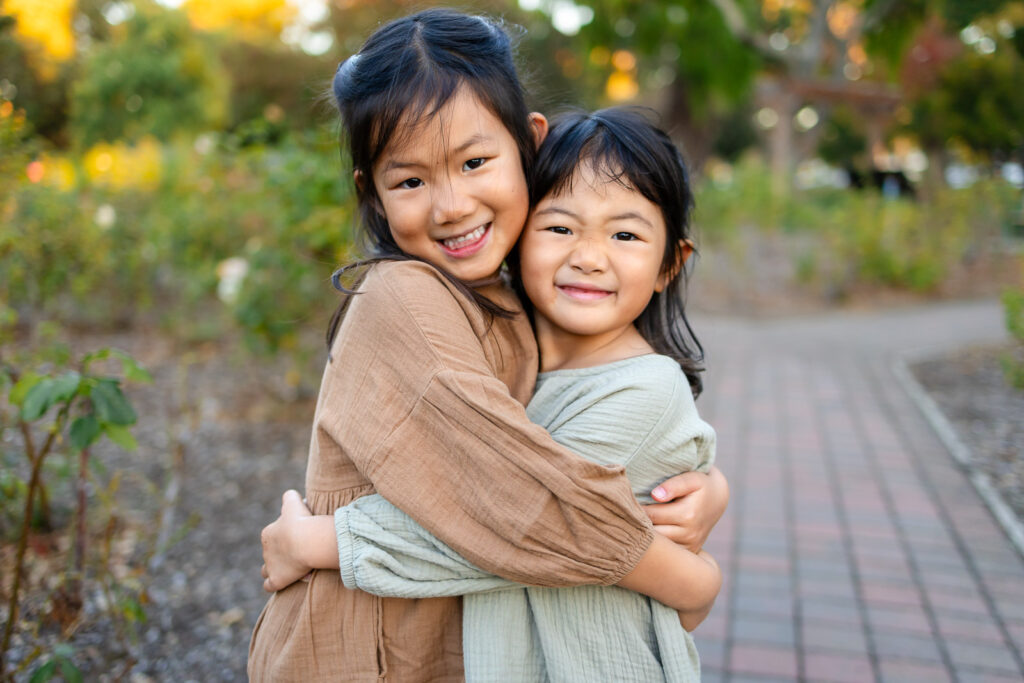 Two sisters hugging on a Burlingame park path for tips for family photos with toddlers