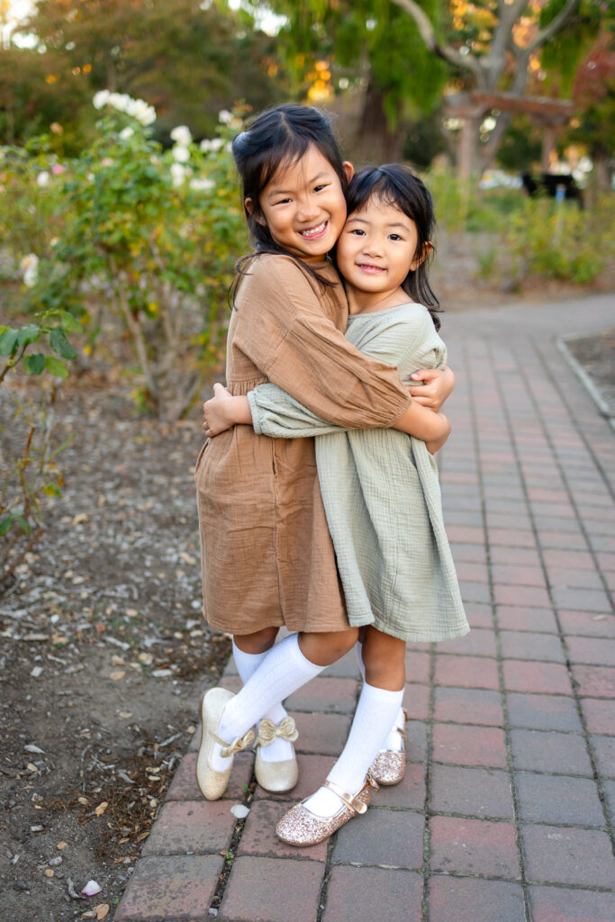 Sisters embracing in a rose garden for tips for family photos with toddlers