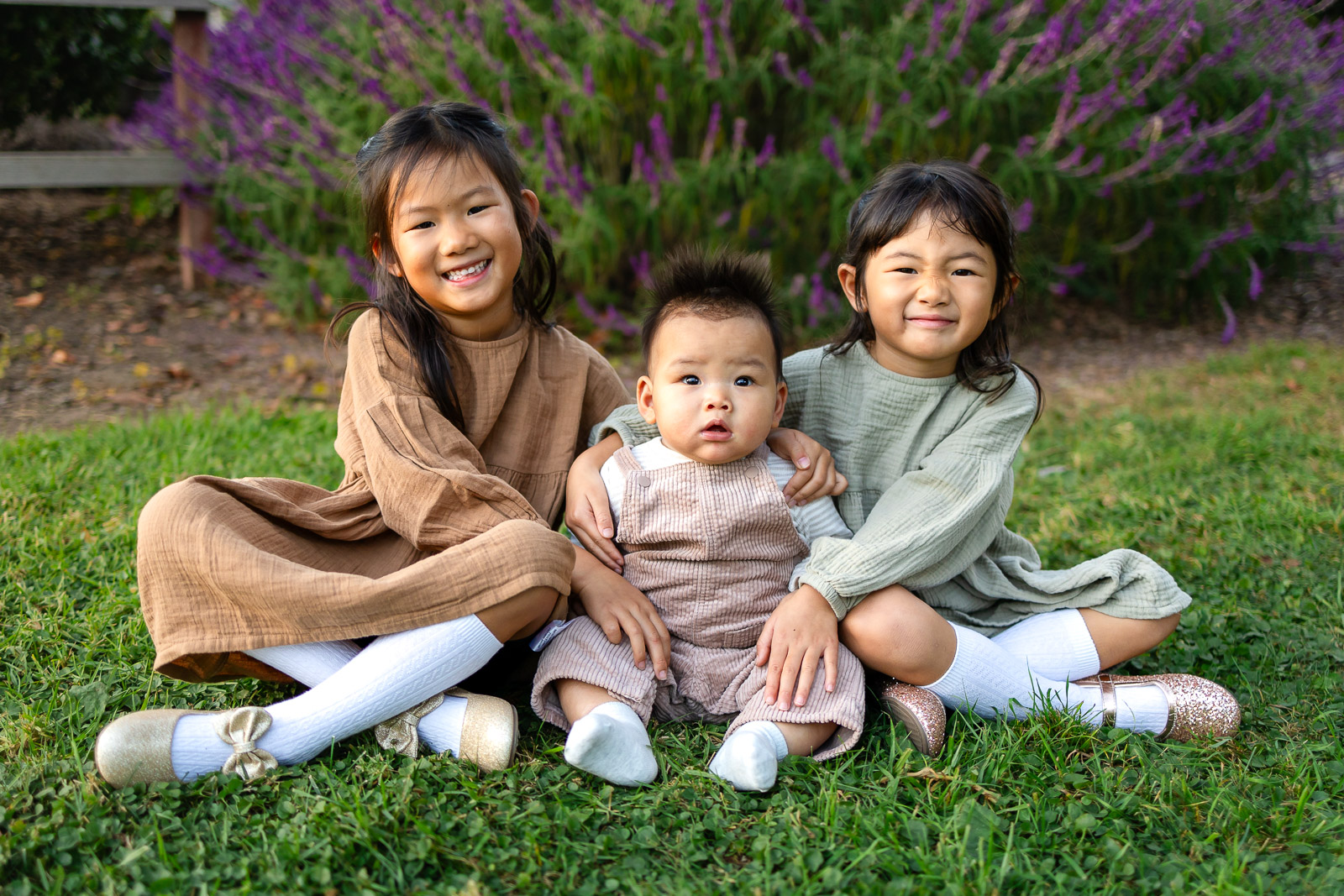 Three siblings sitting on green grass at a park for tips for family photos with toddlers – Ellobelle Photography