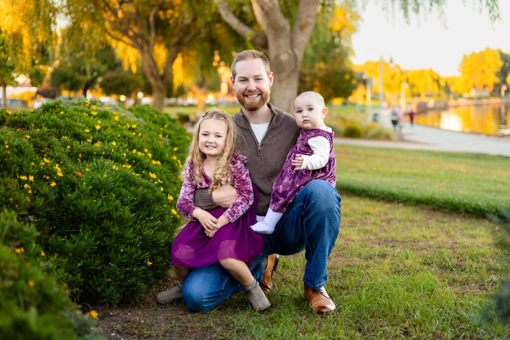 Dad sitting with his two daughters near the gardens at Leo Ryan Park for a what to bring to a photoshoot guide