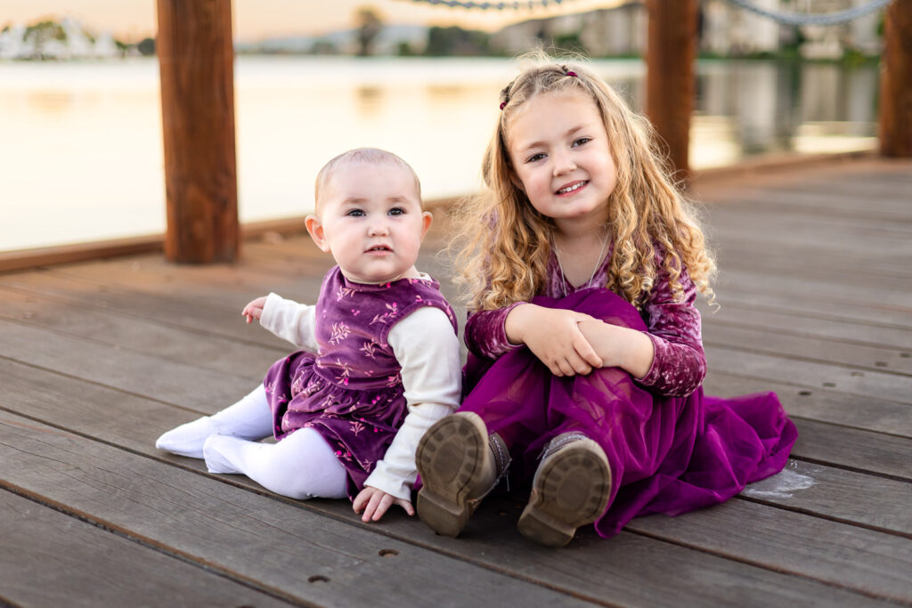 Sisters sitting together on a wooden boardwalk beside a San Mateo lake for a what to bring to a photoshoot post