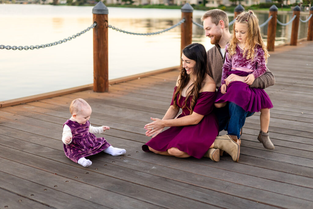 Family sitting on a lakeside boardwalk at a San Mateo park while baby explores