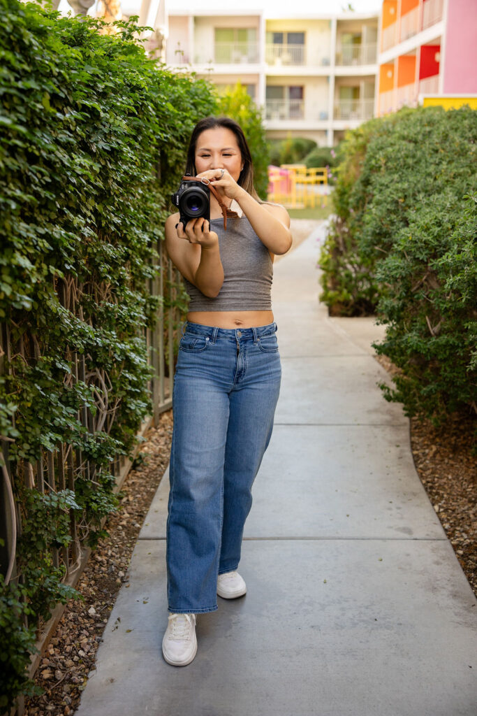 A Bay Area photographer focused on real life moments pauses mid walk on an outdoor path holding her camera at chest height