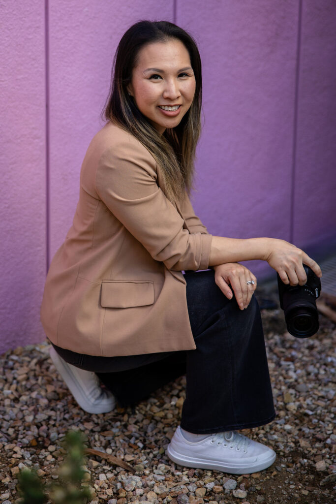 A photographer crouches near the ground holding a camera, smiling calmly in a natural light portrait that reflects a Peninsula lifestyle photographer.