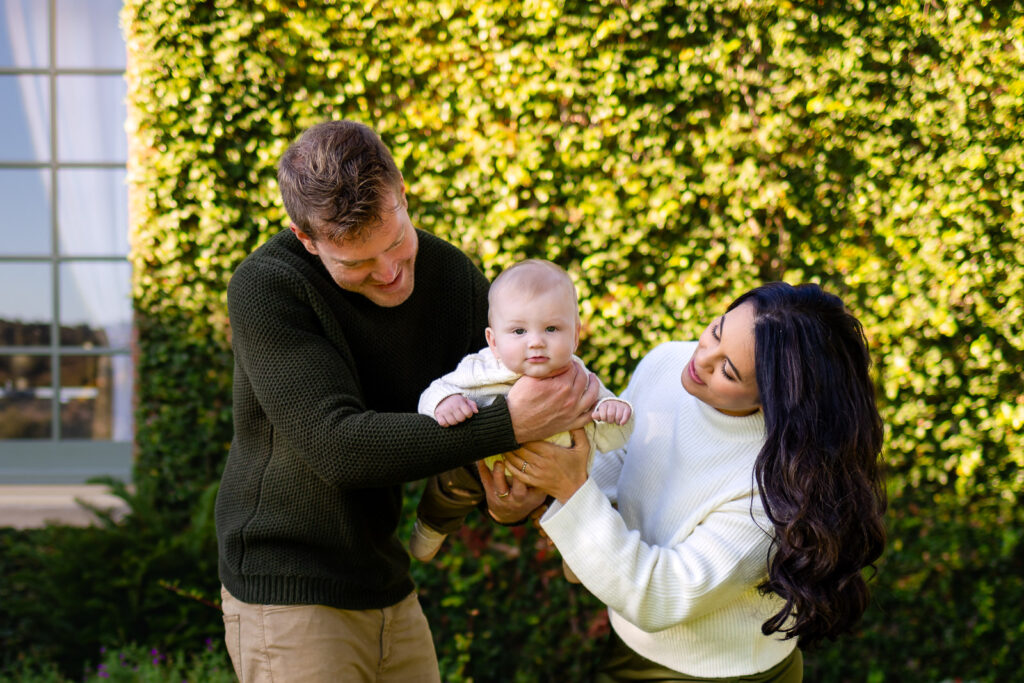 Parents play with their baby together between them, smiling and laughing during a relaxed Bay Area lifestyle photographer session.