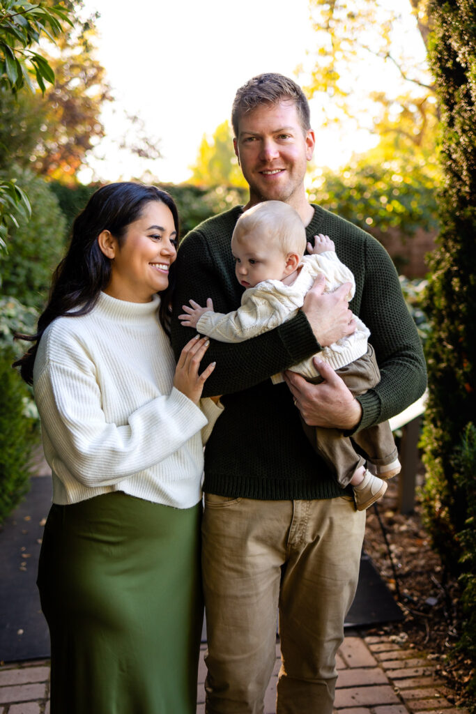 Parents walk hand in hand down a garden path while the mother holds their baby, photographed by a Bay Area lifestyle photographer.