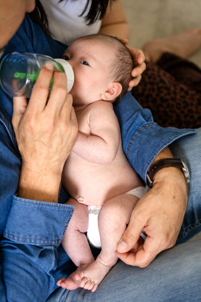 A close up of a newborn being bottle fed while cradled in a parents arms during newborn photos at home.