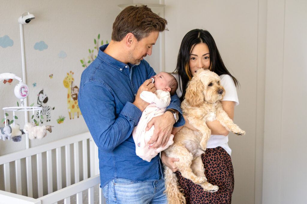 A father holds the newborn while the mother cradles their dog inside the nursery during an in home newborn session.