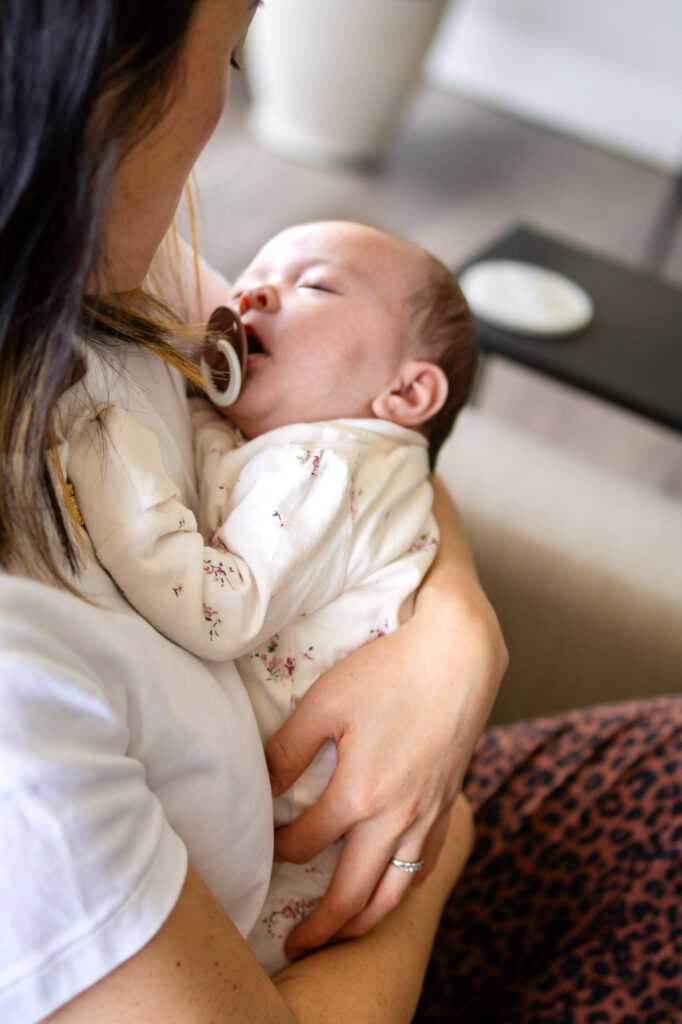 A newborn sleeps peacefully against their mother’s shoulder while being held during a relaxed in home newborn session.