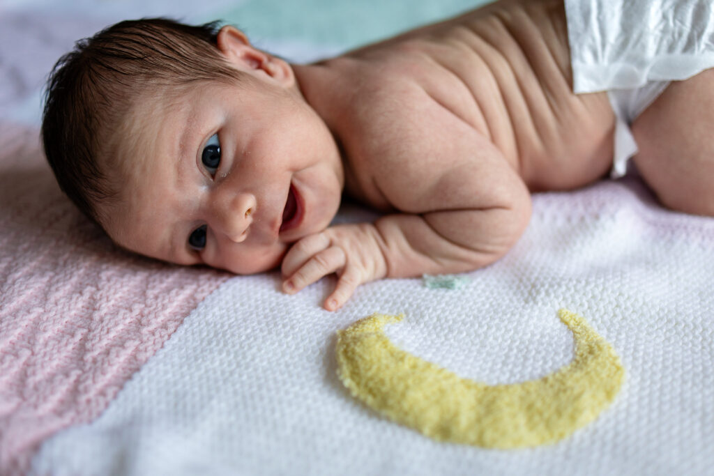 Close up of a newborn lying on their side on a blanket, wide eyed and alert, showing tiny details and soft expressions.