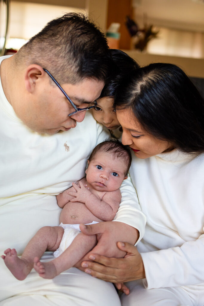 Parents lean in close with their older child to admire their newborn, capturing a tender connection between siblings and parents.