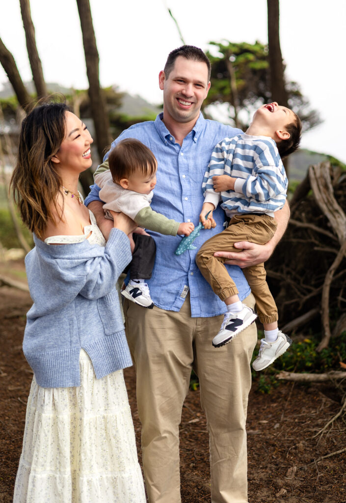 Both parents hold their children while laughing together as the toddler throws his head back in delight during a relaxed and guided family session.