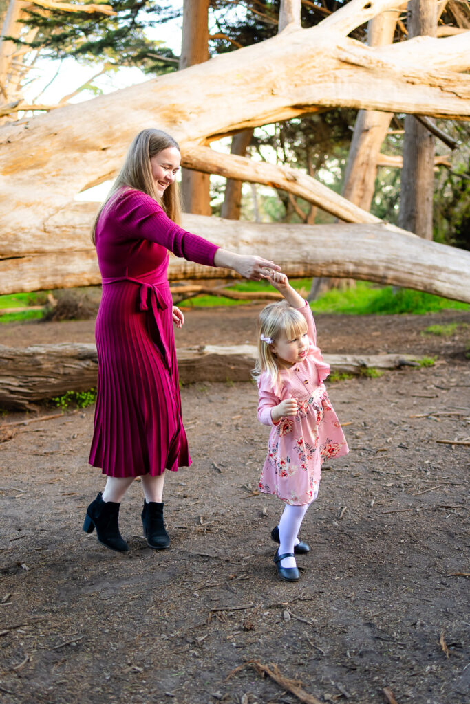 A mother twirls while holding hands with her husband and daughter, creating playful movement during coastal family photography in Half Moon Bay.
