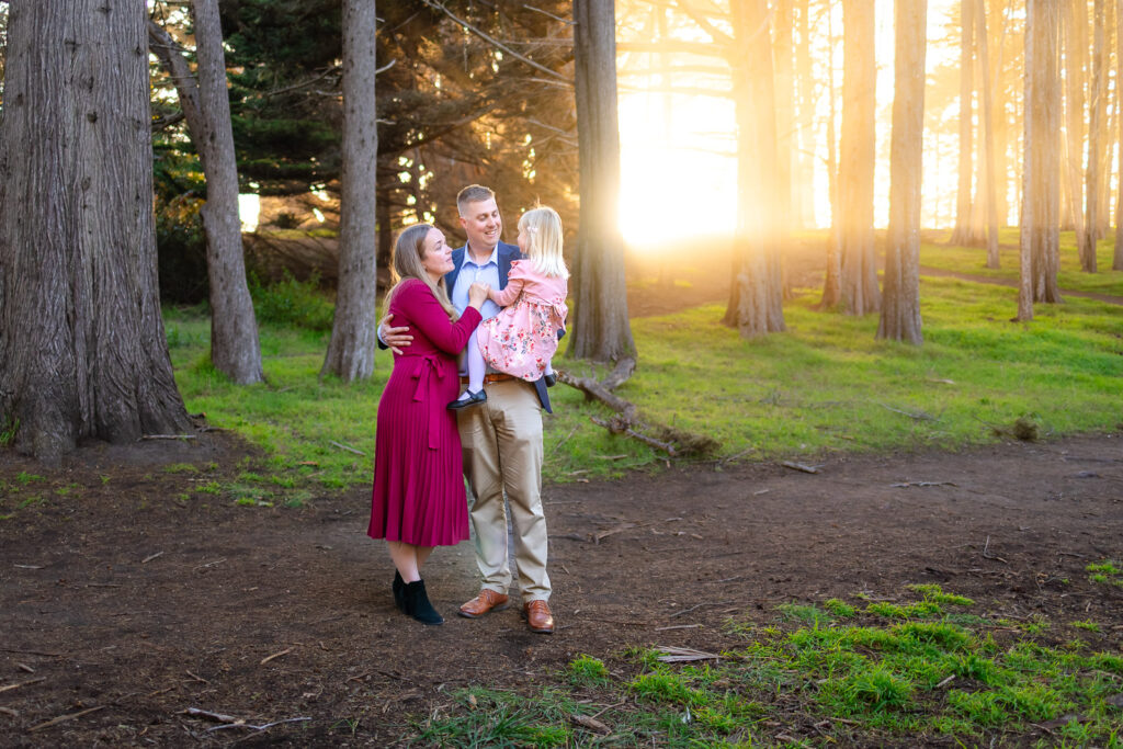 A wide portrait of a family standing together beneath tall cypress trees as the sun sets behind them, captured by a Peninsula photographer