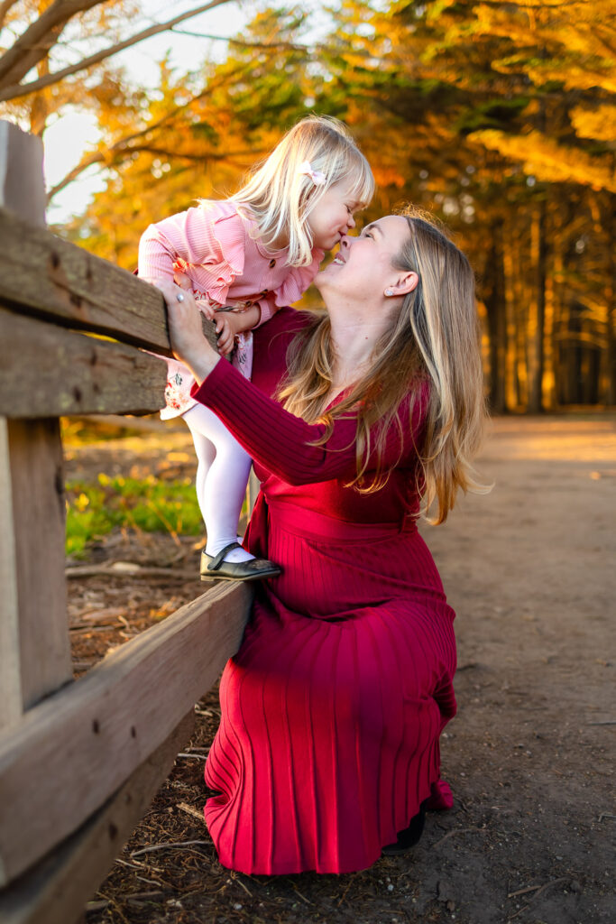 A mother and daughter share a gentle nose to nose moment by a wooden fence, photographed by a Half Moon Bay family photographer.