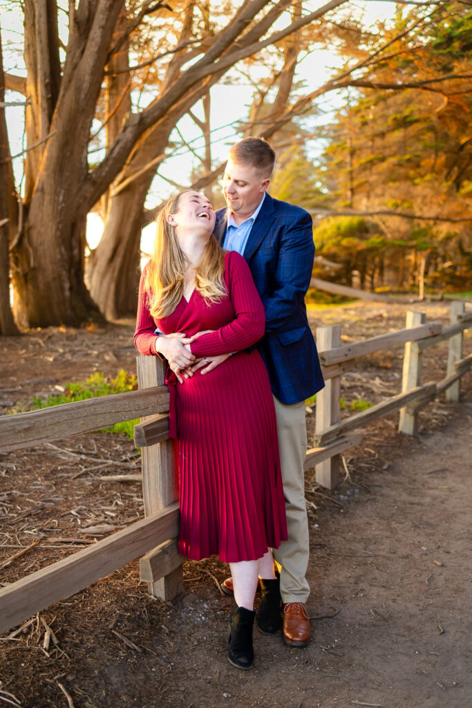 A couple stands close together with the father’s arms wrapped around the mother as they smile toward the camera