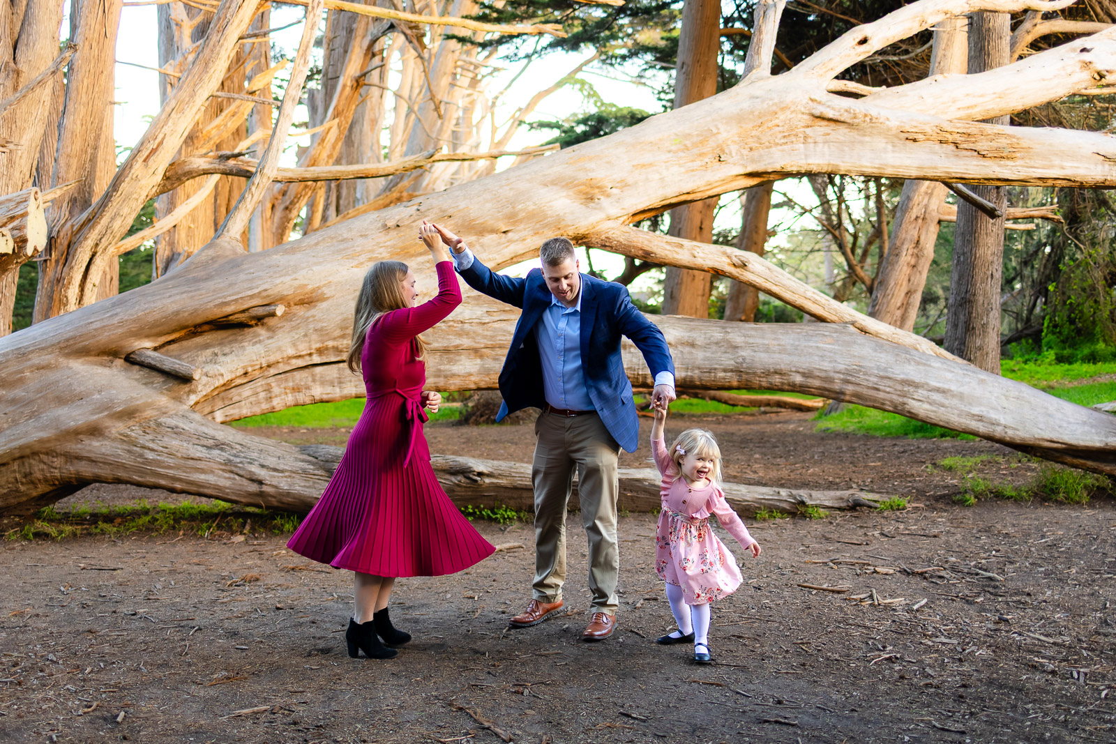 A mother twirls while holding hands with her husband and daughter, creating playful movement during coastal family photography in Half Moon Bay.