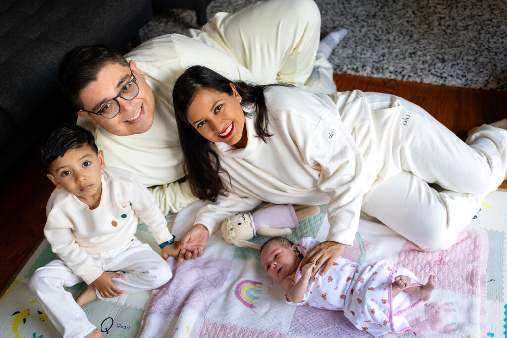 Family of four gathered on floor for newborn photos with toddlers in San Mateo County home