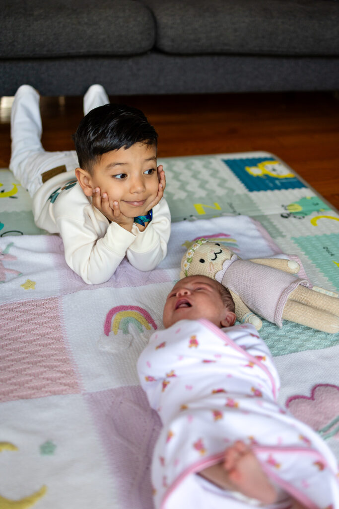 Toddler lying beside newborn sibling during newborn photos with toddlers in a relaxed in-home family session