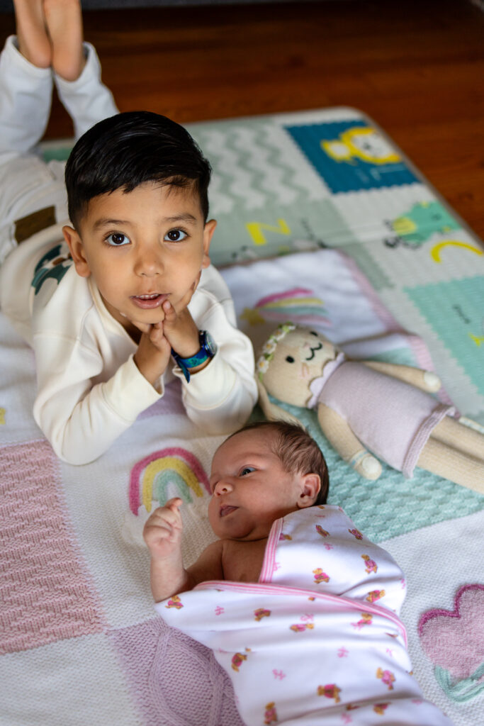 Two year old sibling smiling beside newborn during newborn photos with toddlers using safe floor posing