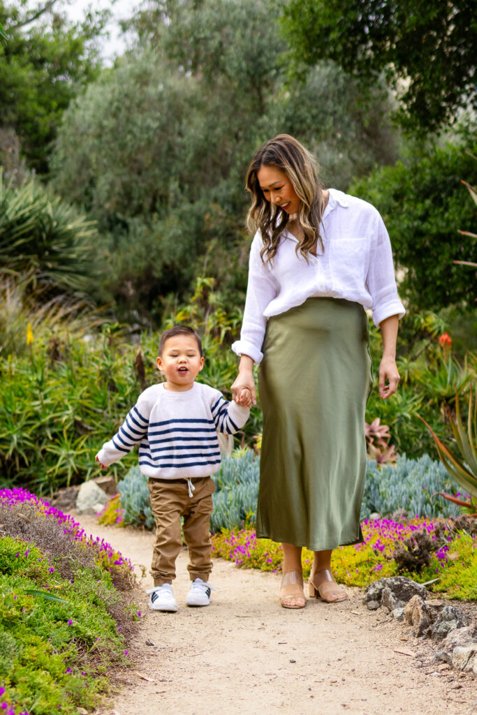 A mother walks hand in hand with her toddler along a winding path surrounded by greenery at one of the family photo locations.