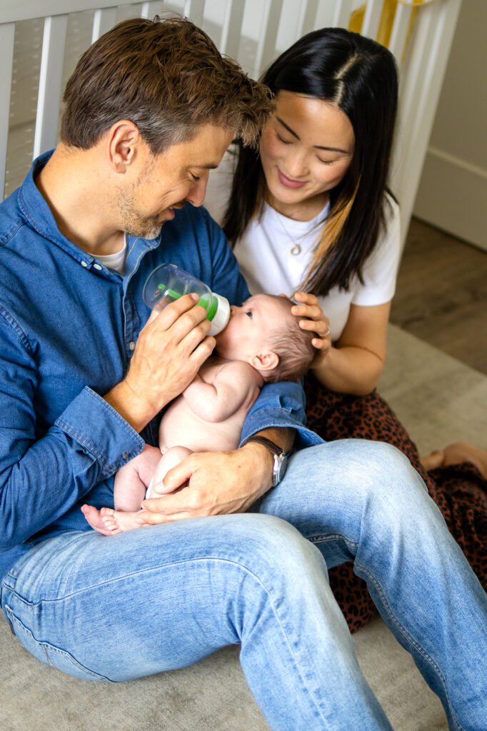 Close up of a newborn baby drinking from a bottle while cradled in their father’s arms, showing the detail and care involved in lifestyle newborn photography and What Affects the Cost of Newborn Photography in the Bay Area.