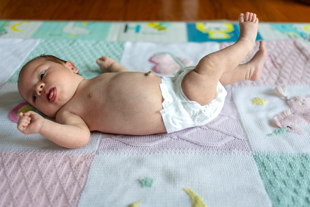 Parents lying on a play mat beside their newborn and toddler smiling toward the camera.