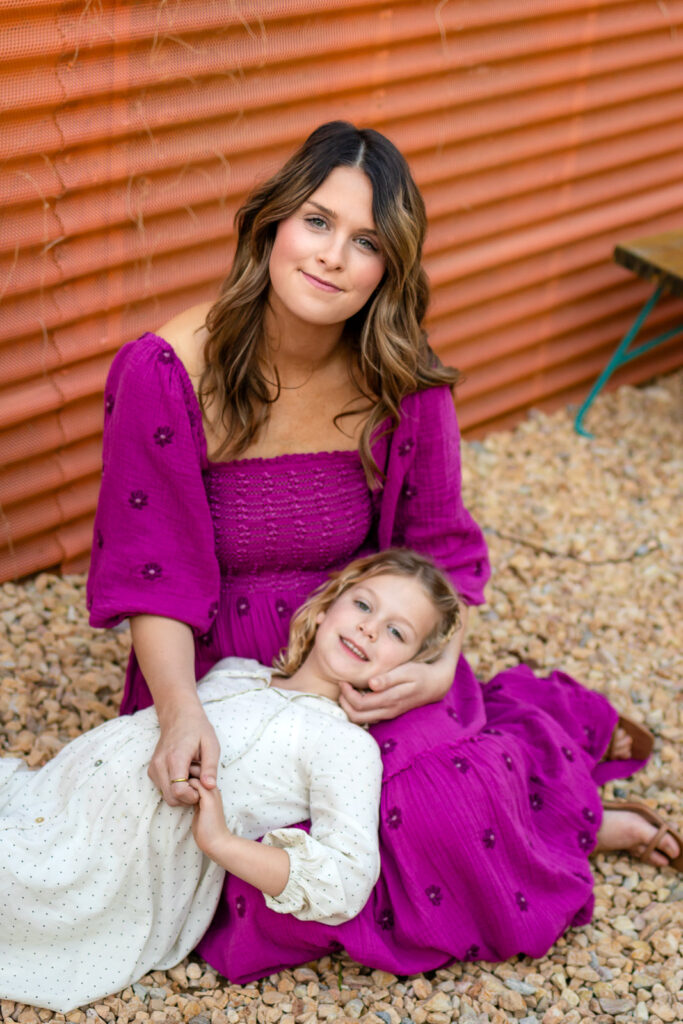 Mother sitting on gravel while daughter hugs her from behind during Motherhood mini sessions Peninsula outdoor lifestyle portrait