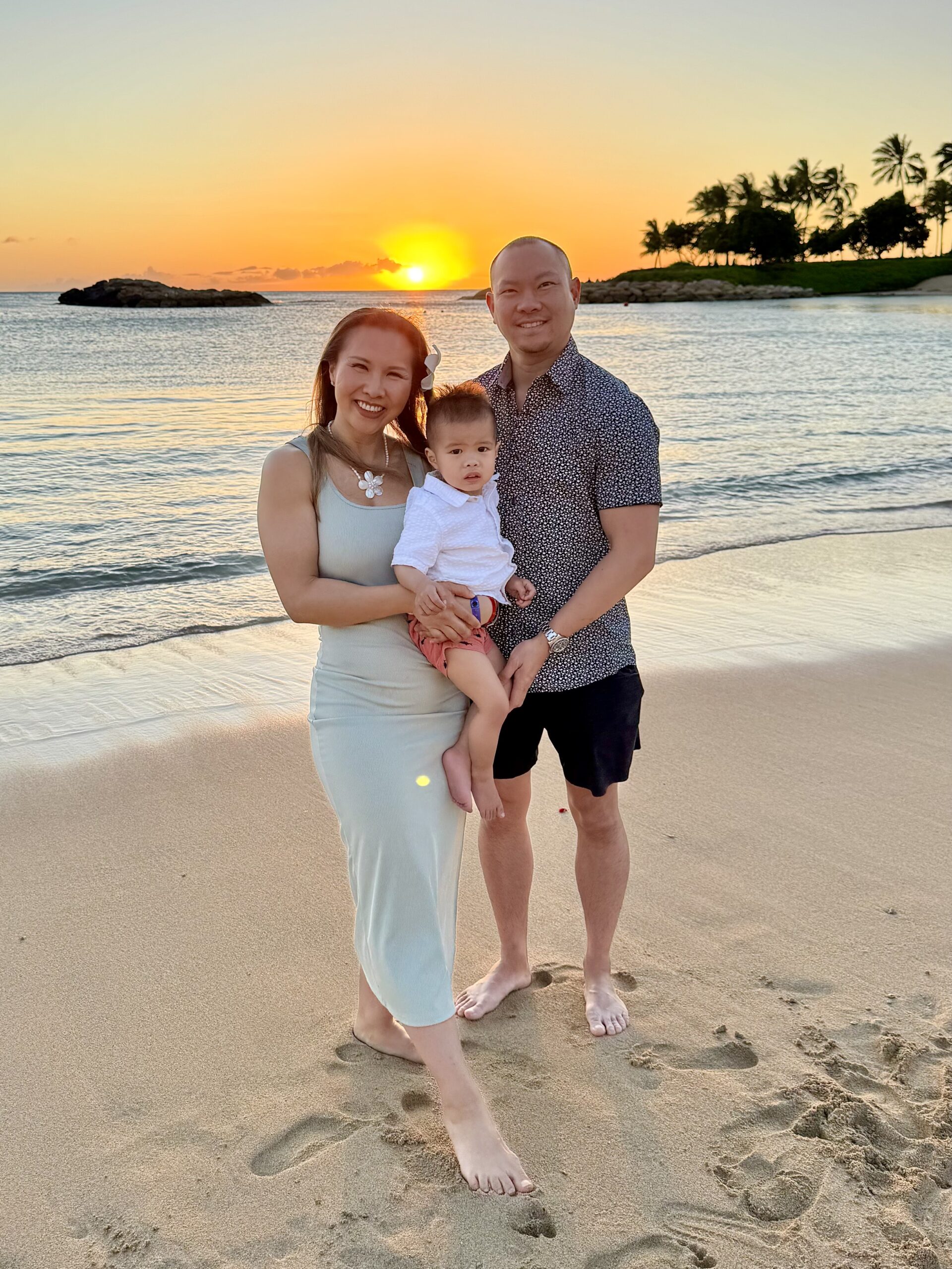 A family standing on a sandy beach during a vibrant golden hour sunset, showing the beautiful results of timing family portraits with iPhone during the best light.