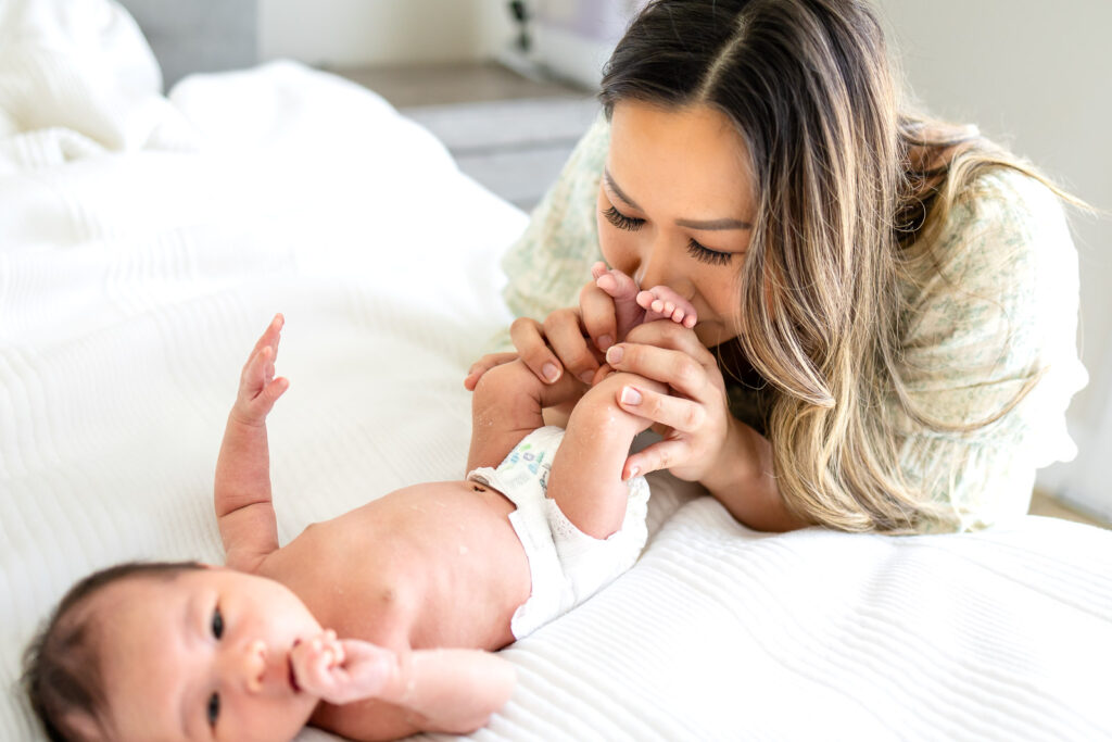 A first-time mother gently cradles her newborn baby on a bed during an in-home session, illustrating the calm and connection-driven approach of Ellobelle Photography.