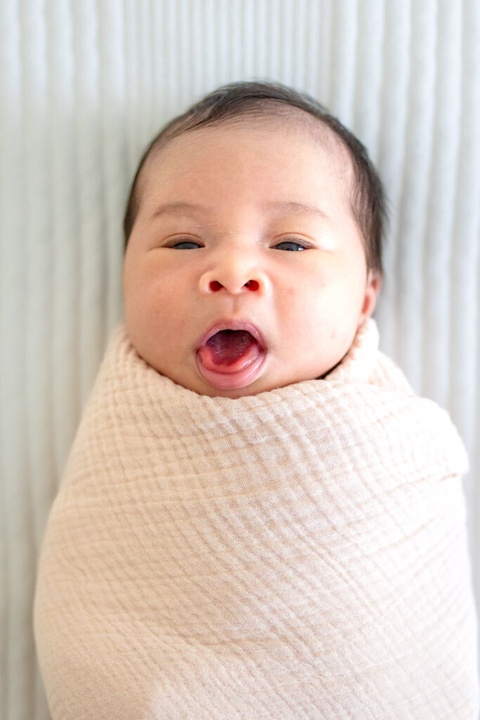 A first-time mother and father smiling warmth with their newborn baby in a light-filled San Francisco Peninsula bedroom, showcasing a stress-free and guided in-home photography experience.