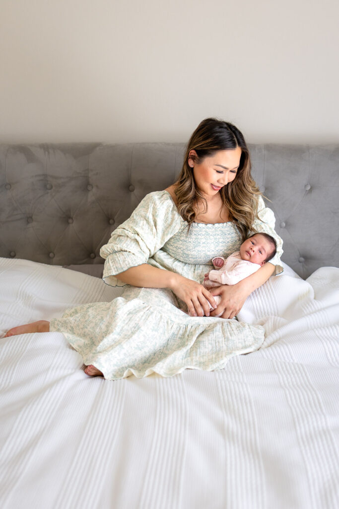 A first-time mother gently cradling her newborn baby on a bed, illustrating the calm and connection-driven approach of Ellobelle Photography compared to a structured studio session.