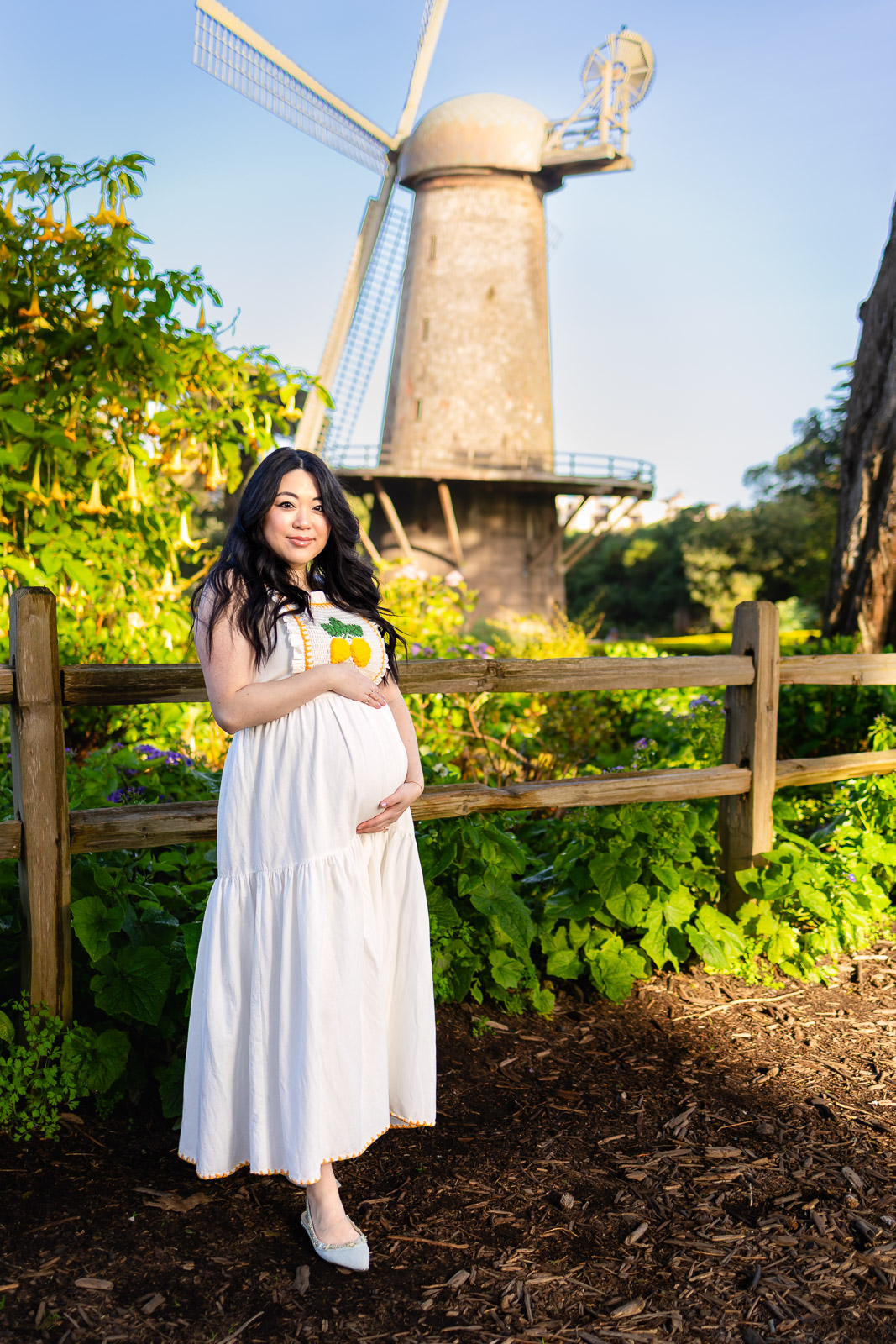 A pregnant woman in a white dress standing in a tulip garden at Queen Wilhelmina Garden, Golden Gate Park.