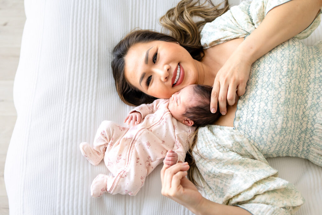 A mother lies comfortably on a soft rug next to her newborn, demonstrating the safe and guided floor posing used in a well-led SF Peninsula family session.