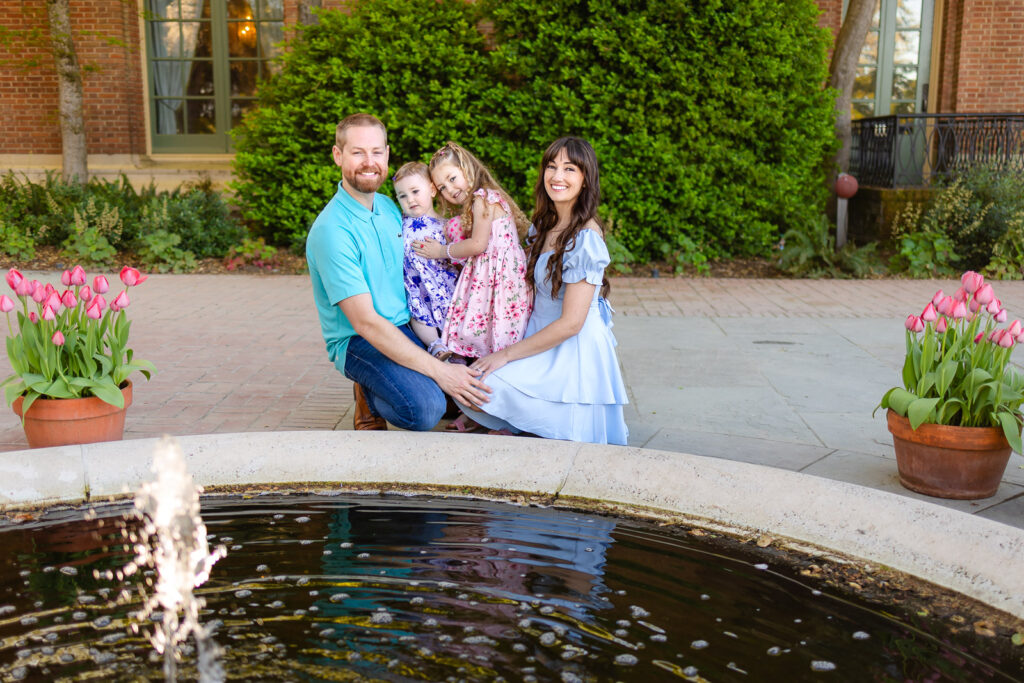 A family sits casually on the grass near a serene stone water fountain, embodying the relaxed family portraits standard at Filoli.