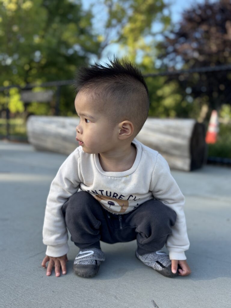 A young boy crouching at eye level outdoors, an example of using iPhone Portrait Mode to create a soft, blurred background for meaningful family photos.