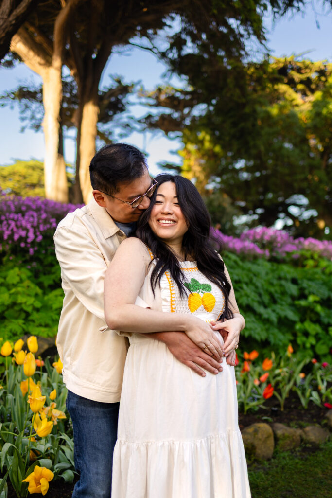 A couple wearing neutral spring outfits standing in golden hour light surrounded by blooming flowers at a San Francisco Peninsula photo session.