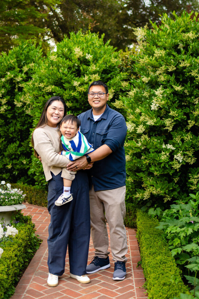 Family of three walking through a formal garden path at Gamble Garden.