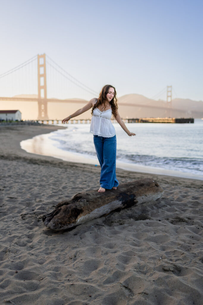 Girl balancing on a driftwood log with the Golden Gate Bridge in Crissy Field beach
