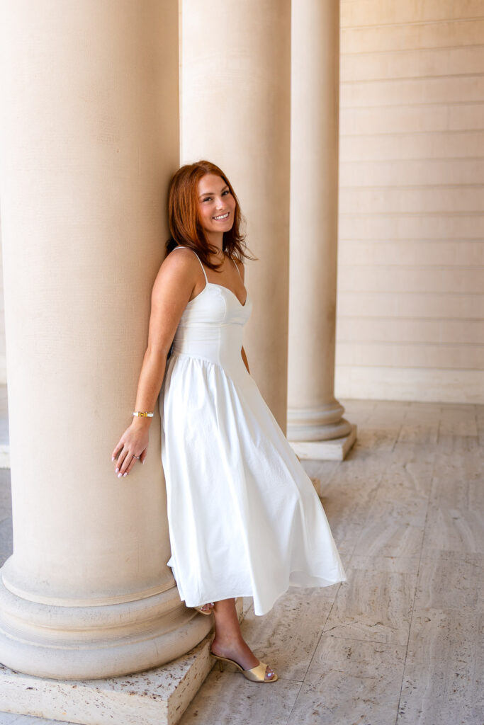 Senior in a white dress leaning against a column at the Legion of Honor, smiling