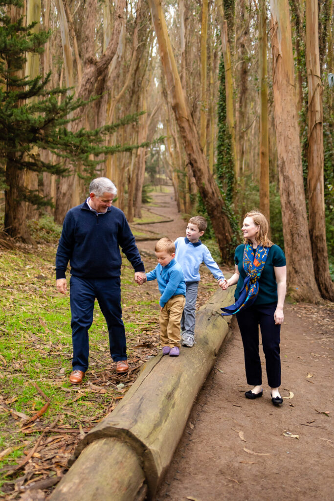 A family balancing on fallen logs in the Presidio forest with a San Francisco family photographer.