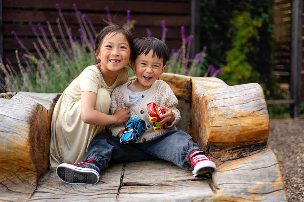 Young siblings brother and sister sitting on a rustic wooden bench surrounded by greenery in Burlingame.