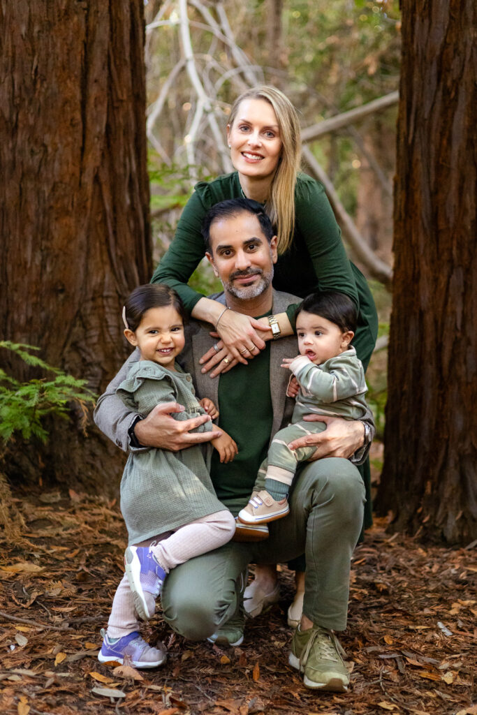 A family of four portrait among redwood trees with soft sunlight filtering through.