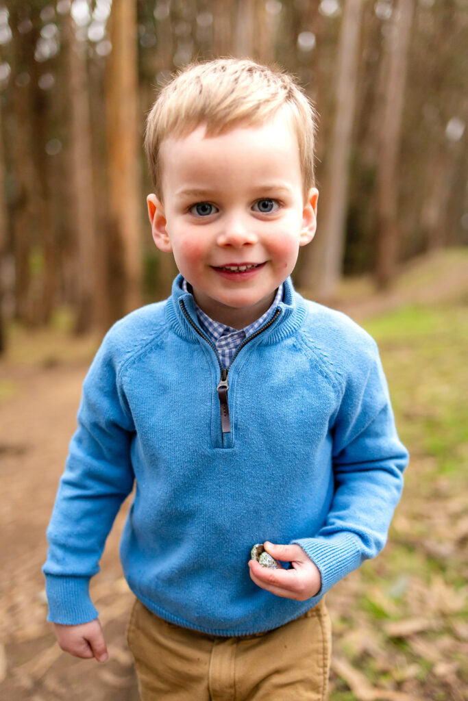 Photographer San Francisco A young boy in a blue sweater smiling in the woods during a San Francisco family photo session.