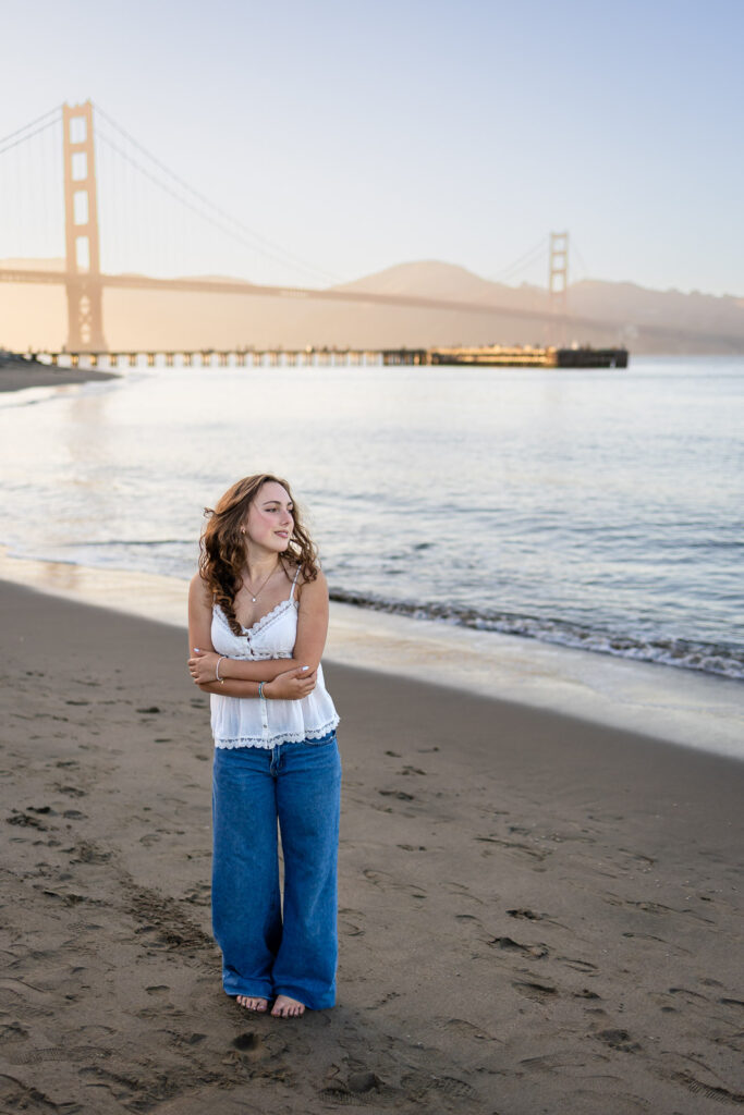 Bay Area mini sessions client standing on the beach in jeans and a white top with the Golden Gate Bridge in the distance