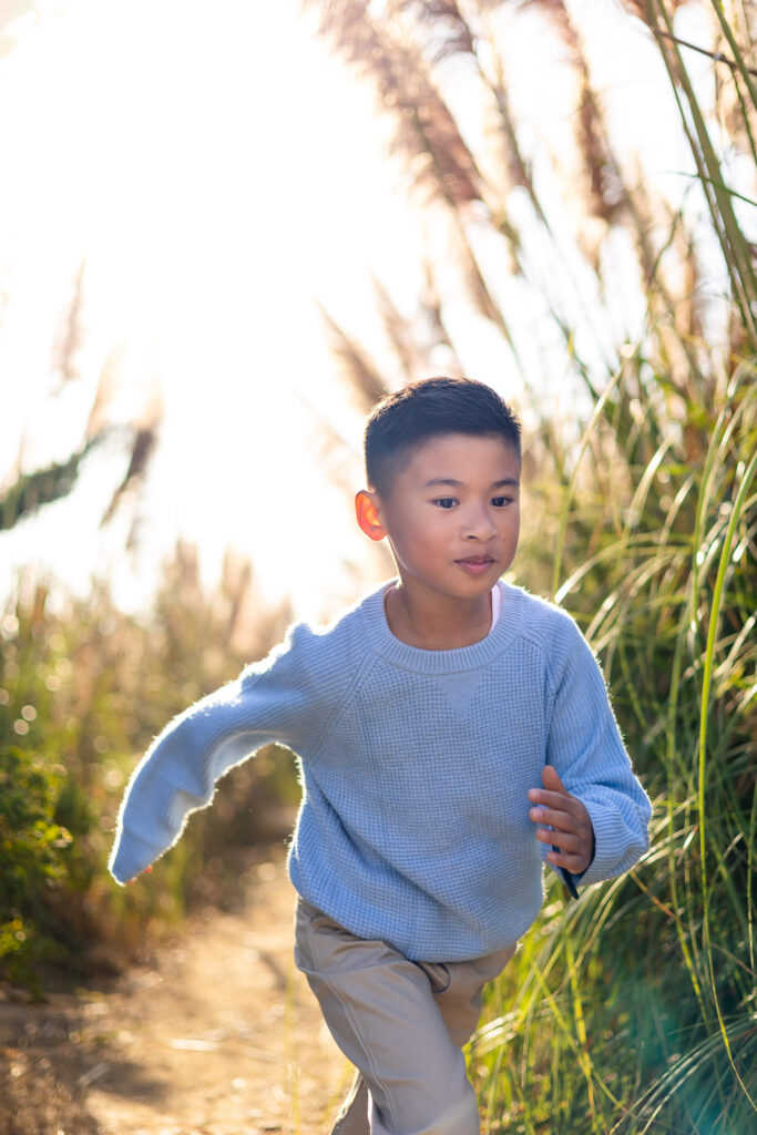 Child running through a sunlit trail surrounded by pampas grass