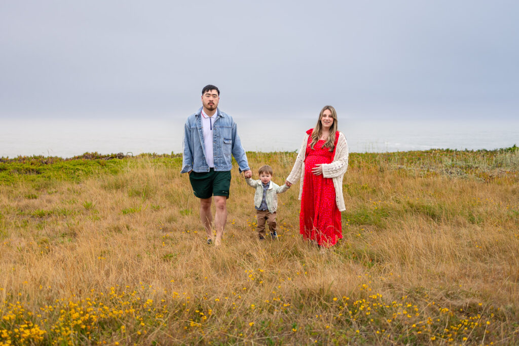 Parents walk together with their young child along the beach during a Half Moon Bay Photographer session.